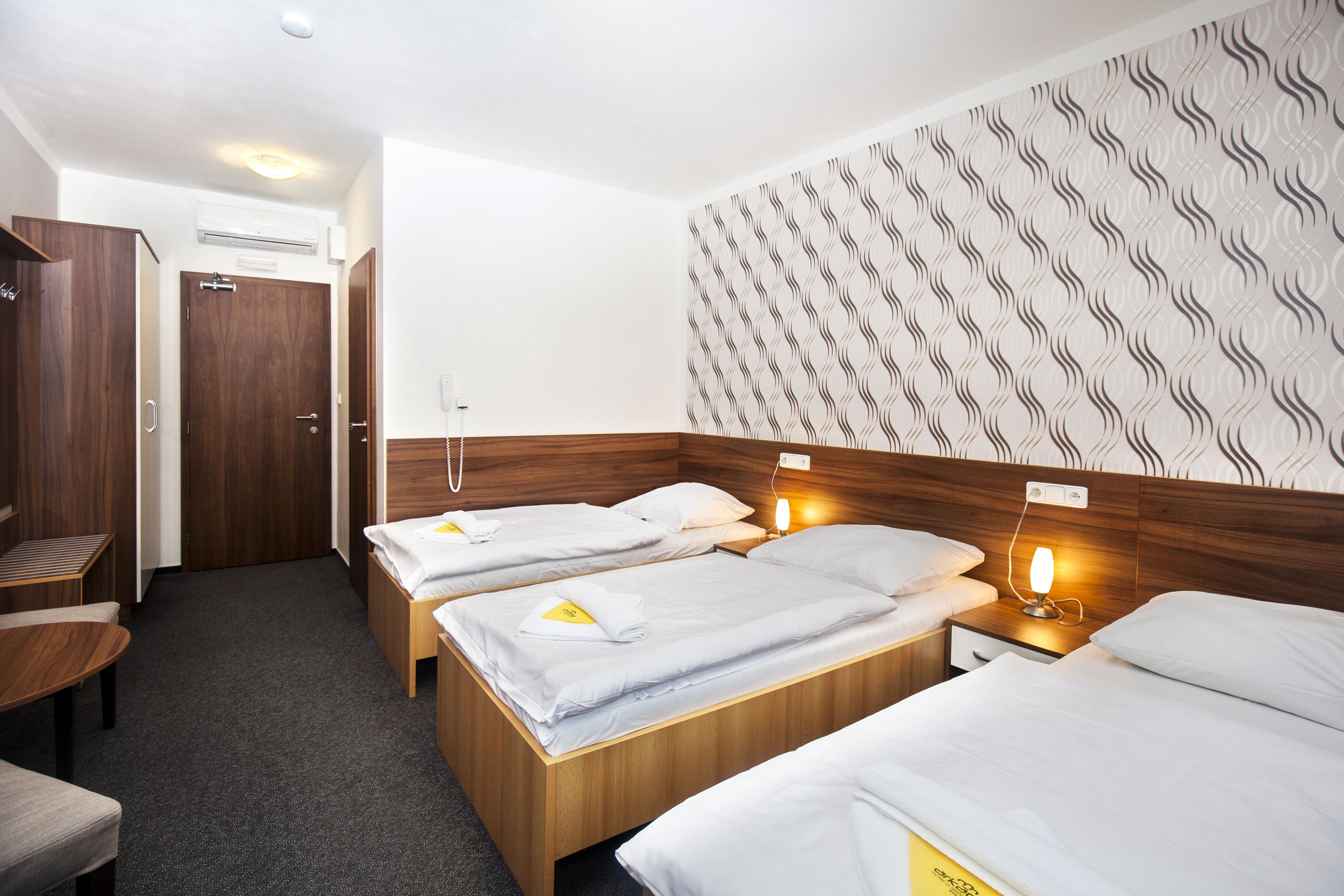 A hotel room with two single beds, a wooden headboard, a patterned wall, and a small table.