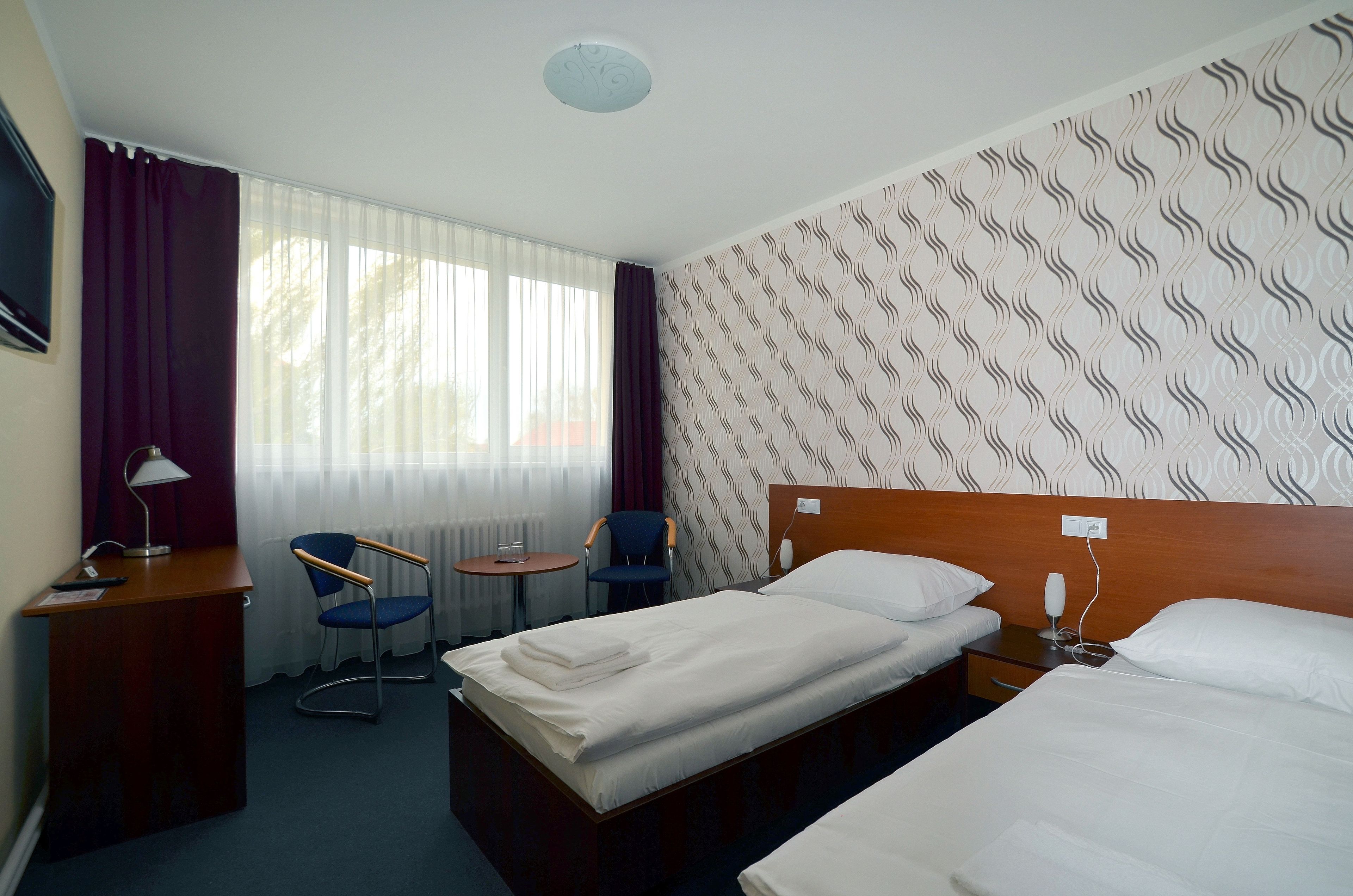 A hotel room with two beds, a desk, a chair, a small table, and a window with curtains.