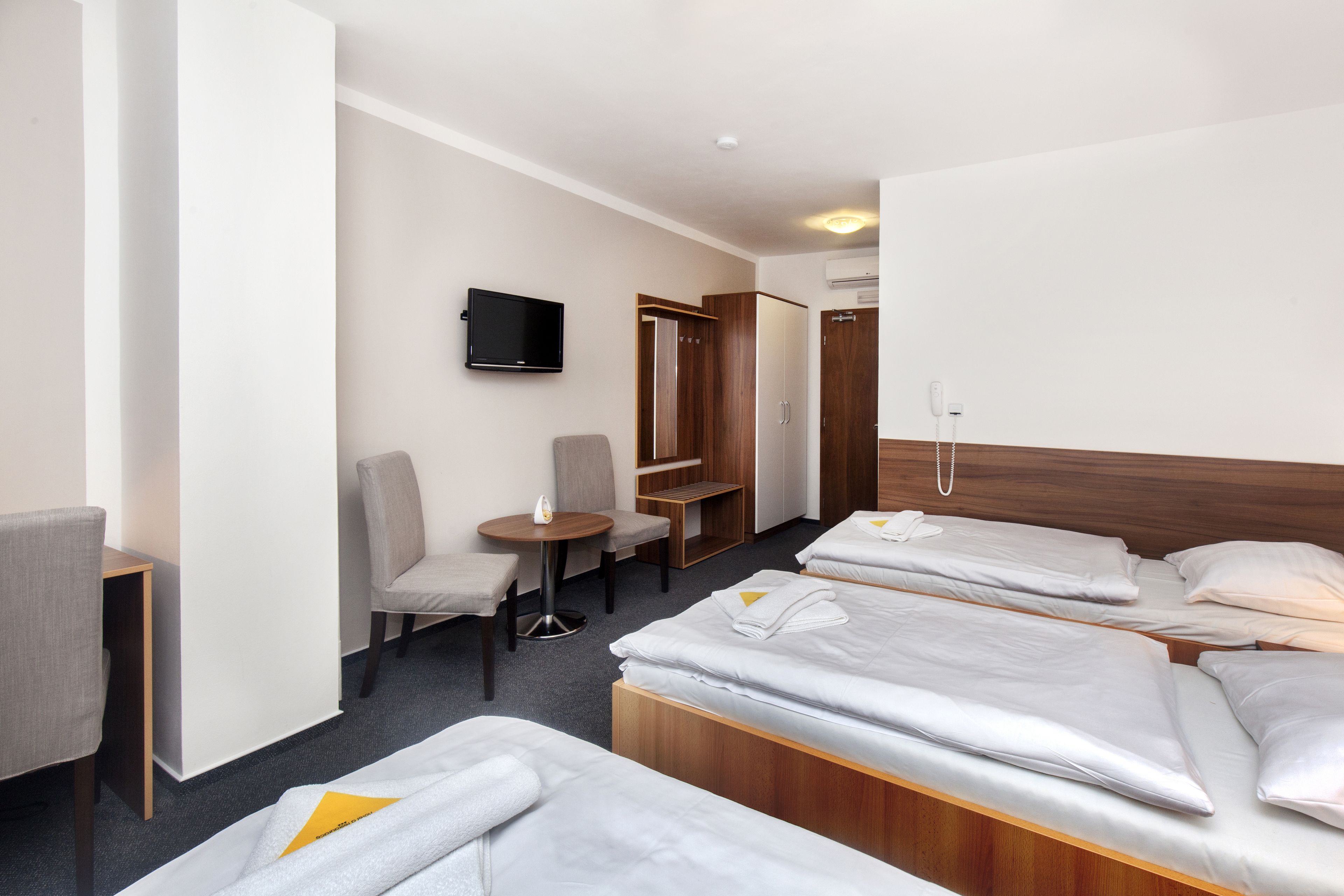 Habitación de hotel con tres camas, televisión, escritorio y una silla.