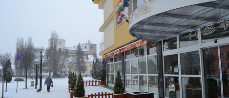 A hotel with a yellow facade, multiple flags, and a covered entrance.