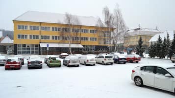 A snow-covered parking lot with several cars and a yellow building in the background.
