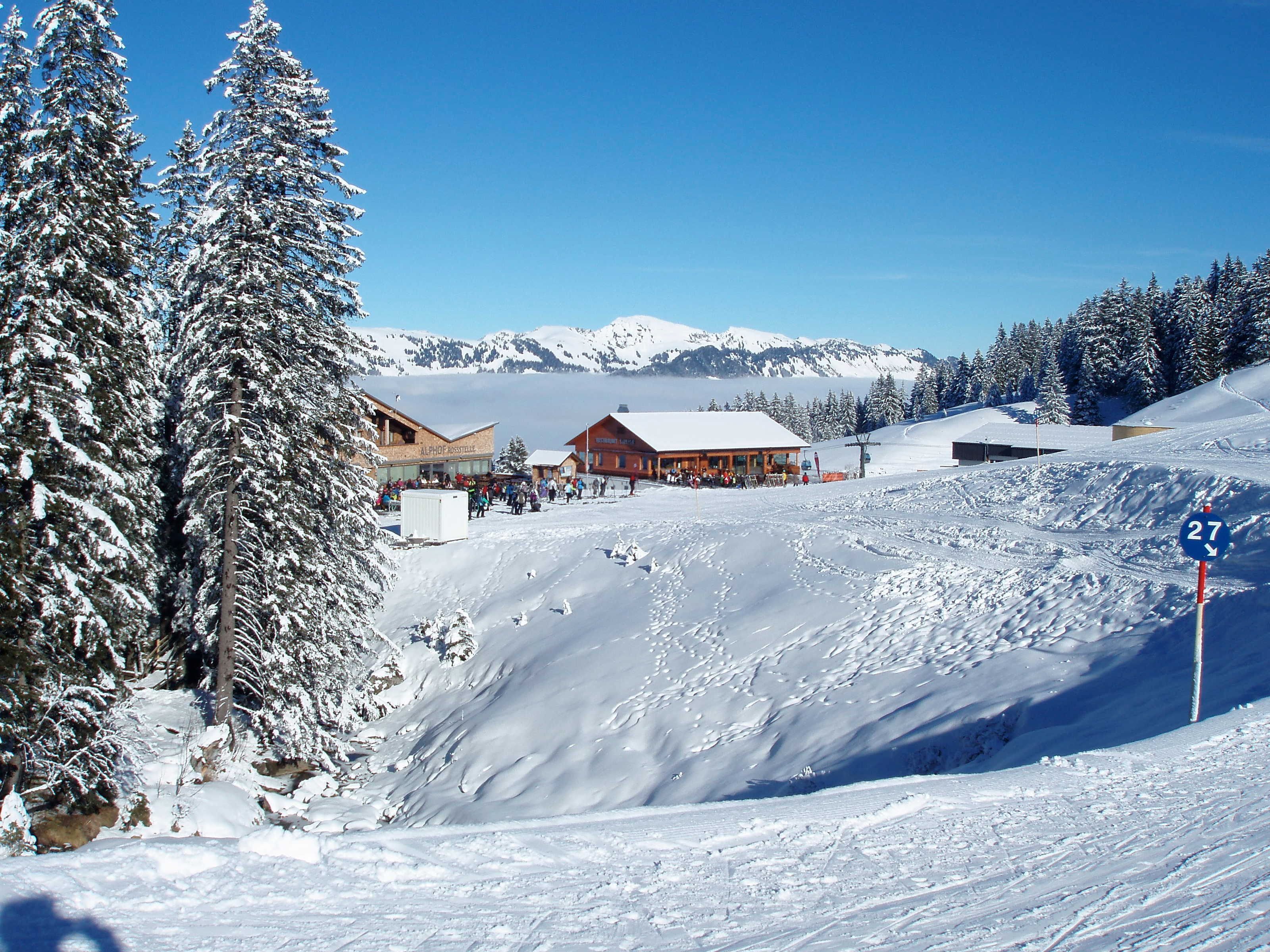A snow-covered ski resort with buildings, a ski lift, and a mountain in the background.