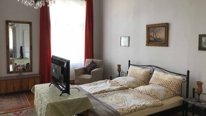 Ein Schlafzimmer mit einem Bett, einem Fernseher auf einem Tisch, einem Sessel, einer Chandelüster und zwei gerahmten Bildern an der Wand.