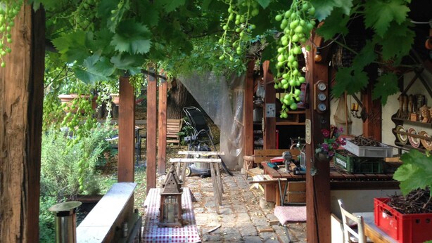 Ein rustikaler Außenbereich mit einer Holzpergola, einem Kiesweg und einem kleinen Tisch mit Stühlen.