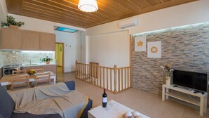 A modern living room with a sofa, a dining table, a TV on a stand, and a kitchen area in the background. - Castello Di Porto (Mylopotamos)