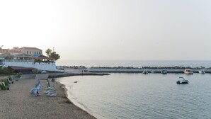 A beach with a row of sun loungers and umbrellas, a pier with buildings, and several boats in the water. - Castello Di Porto (Mylopotamos)