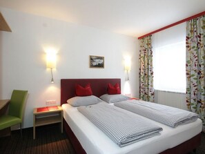 A hotel room with a double bed, two bedside tables, a green chair, and a window with curtains.