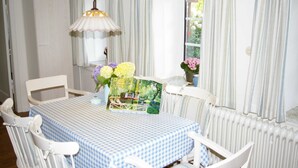 A dining area with a checkered tablecloth, white chairs, a hanging light fixture, and a window with curtains. - Holiday home Klookris 15 (Risum-Lindholm)
