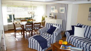A living room with striped sofas, a dining table with chairs, and a wooden coffee table with fruit. - Holiday home Klookris 15 (Risum-Lindholm)