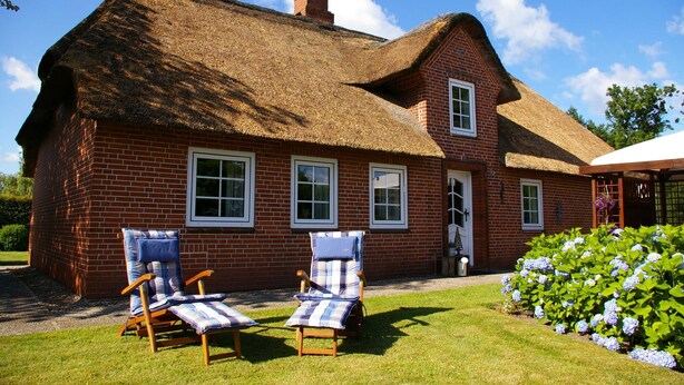 A brick house with a thatched roof, two lounge chairs, and a garden with hydrangeas. - Holiday home Klookris 15 (Risum-Lindholm)