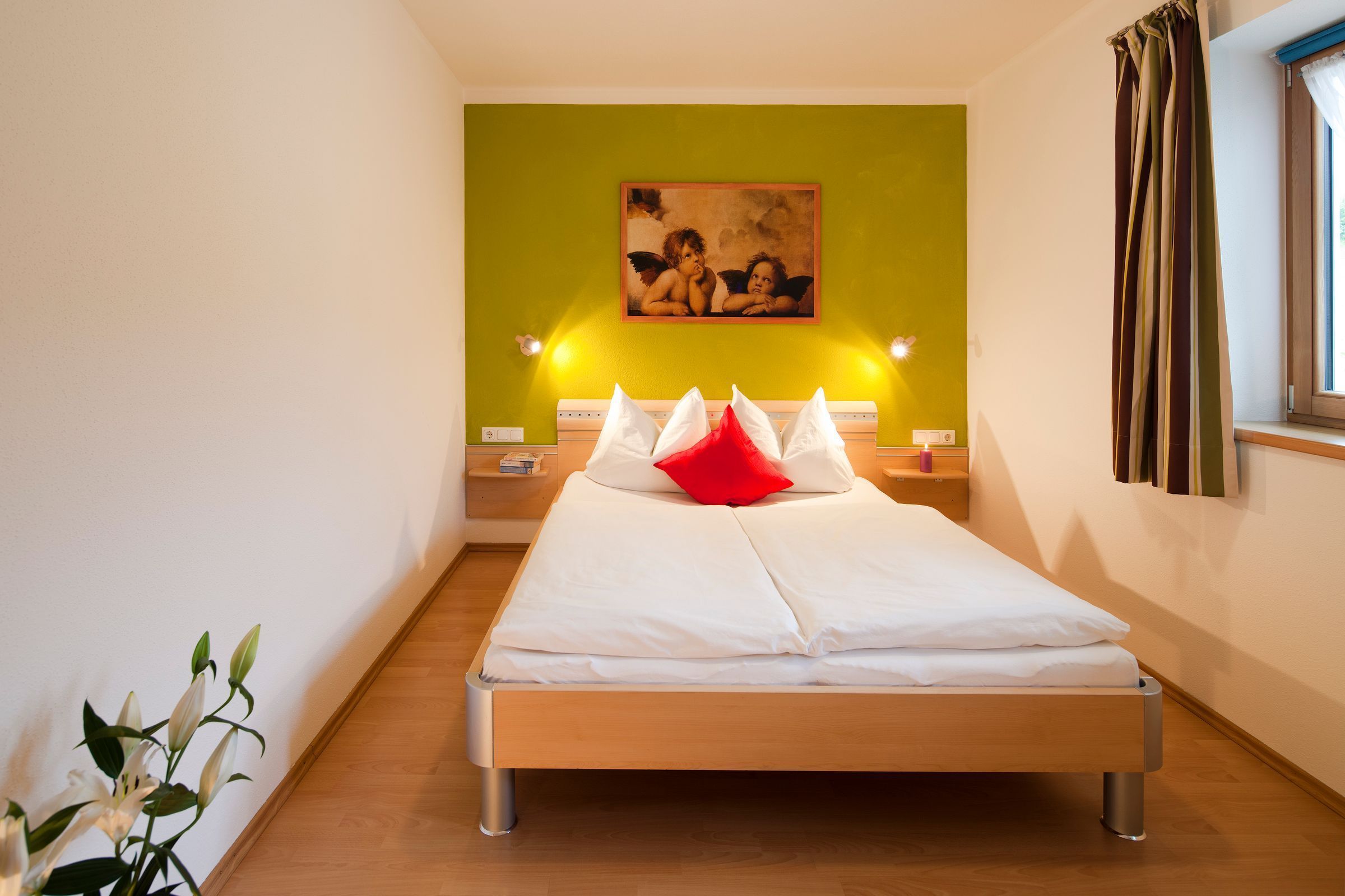 A single bed with white bedding, a green accent wall, and a painting above it.