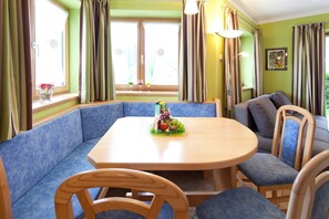 A dining area with a round table, blue cushioned seating, and a fruit centerpiece.