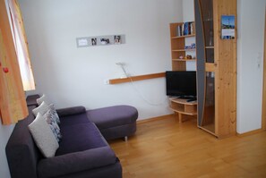 Una sala de estar con un sofá, un televisor, una estantería y una puerta de madera.