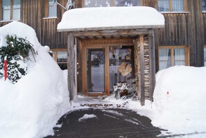 Un edificio de madera con entrada cubierta de nieve y un letrero de madera.