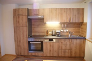 Une cuisine compacte avec des meubles en bois, un four encastré, une machine à café et un évier en acier inoxydable.