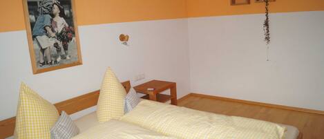 A room with a bed, pillows, a small table, a wall-mounted picture, and a wall clock.