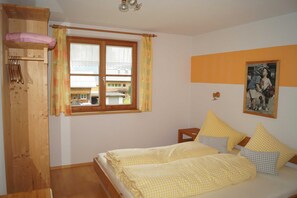 A bedroom with a bed, a wooden wardrobe, a window with curtains, a nightstand, and a wall-mounted picture. - Apartment 1 - Kohler Renate (Schoppernau)