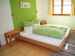 Un lit simple avec une couvre-lit verte, des tables de chevet en bois, un mur vert et une fenêtre avec des rideaux.