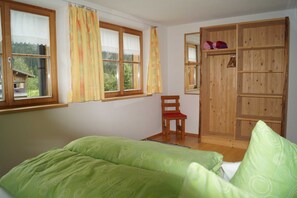Een slaapkamer met een bed, een stoel, een houten garderobe en een raam met gordijnen.