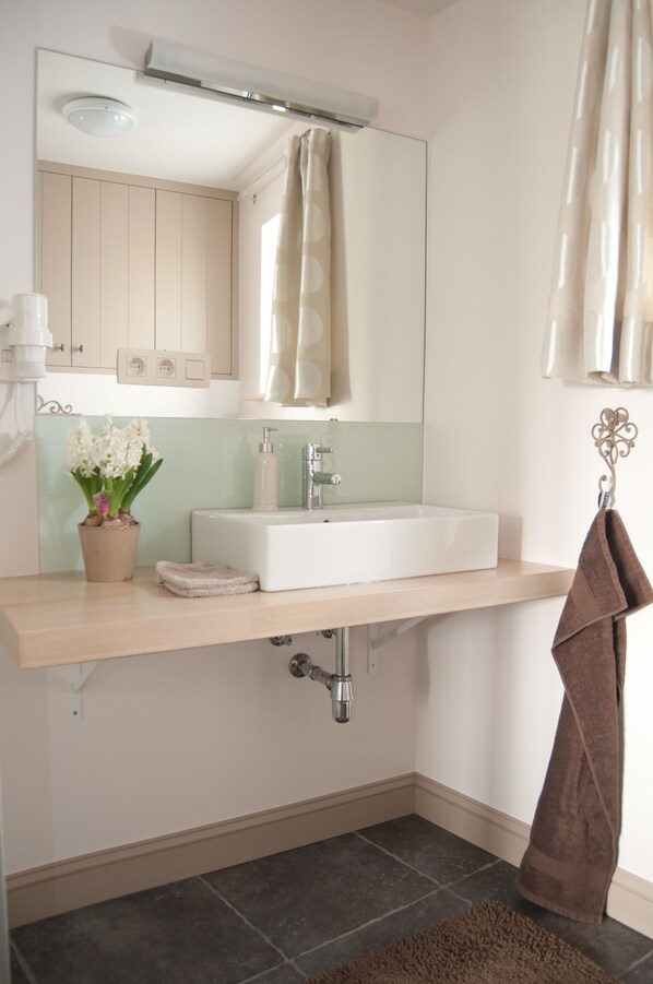 A bathroom with a white sink, a mirror, a towel rack, a potted plant, and a shower curtain. - De Fruithoeve (Hoeselt)