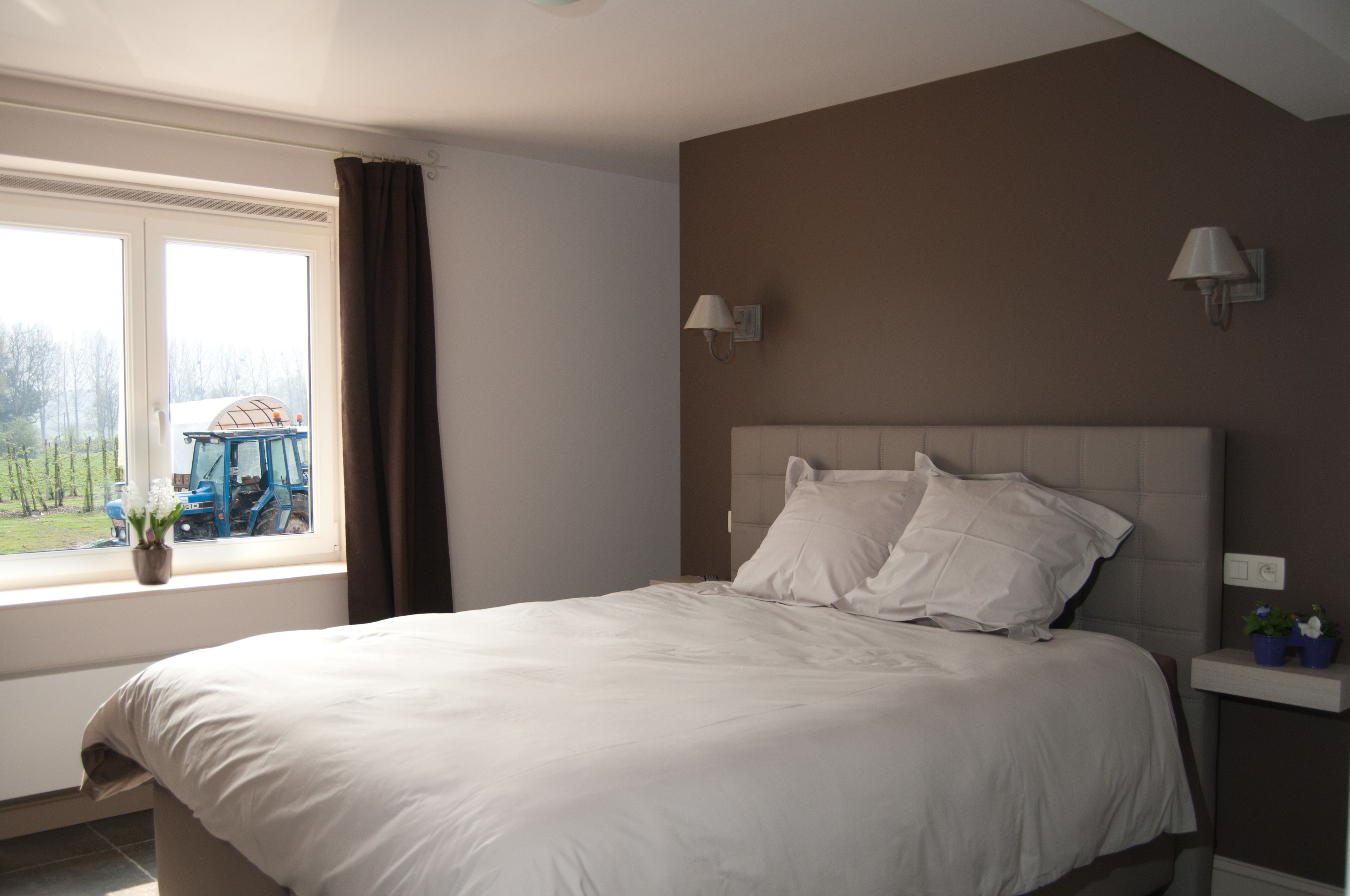 A bedroom with a large bed, a window with curtains, a headboard, and wall-mounted lamps.