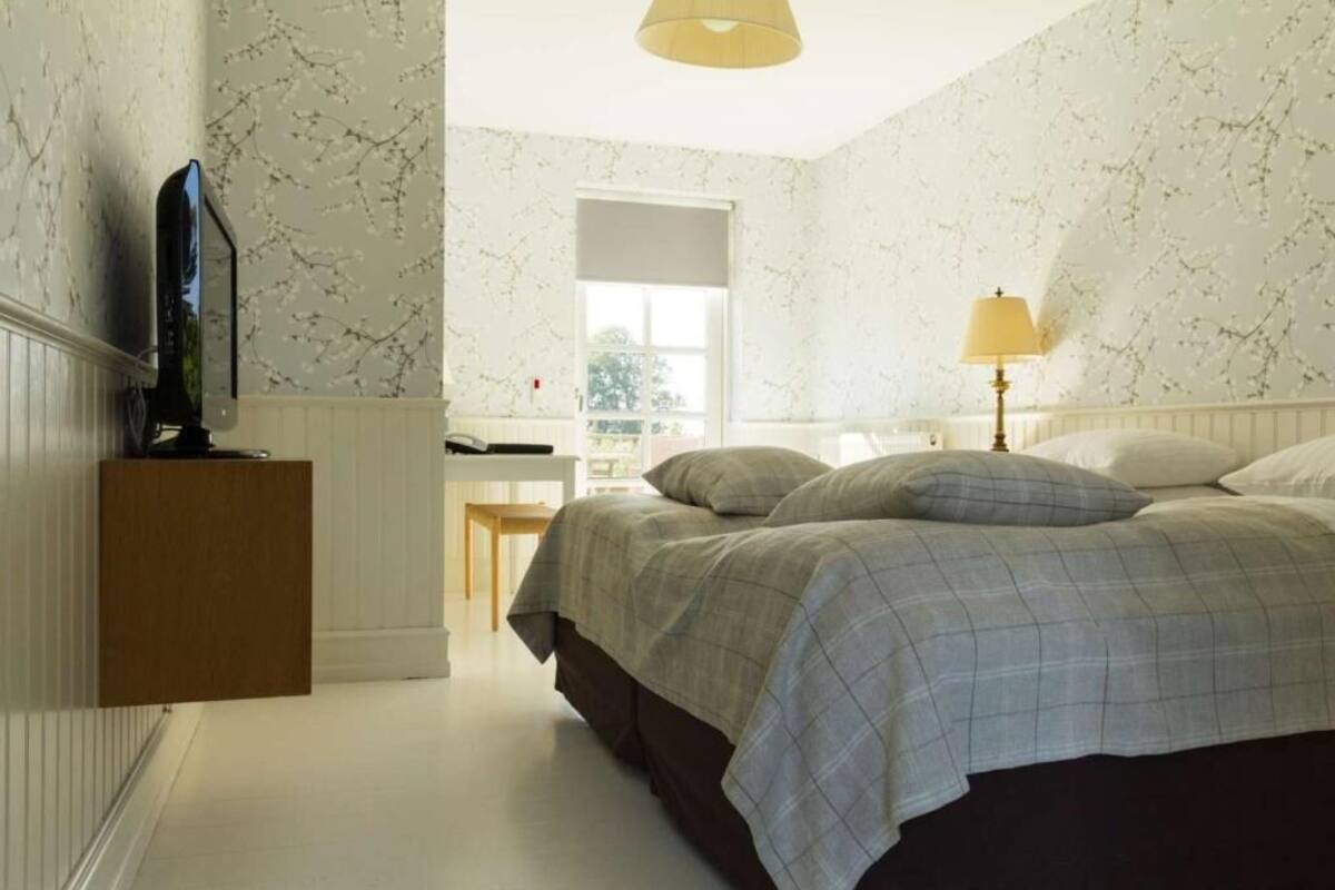 Une chambre à coucher avec un lit, un téléviseur posé sur un meuble, une lampe et une fenêtre.