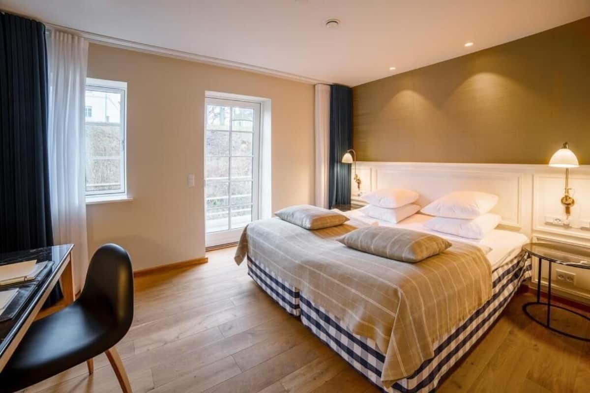Une chambre d’hôtel comprenant un lit, un bureau, une chaise et une table de chevet avec une lampe.