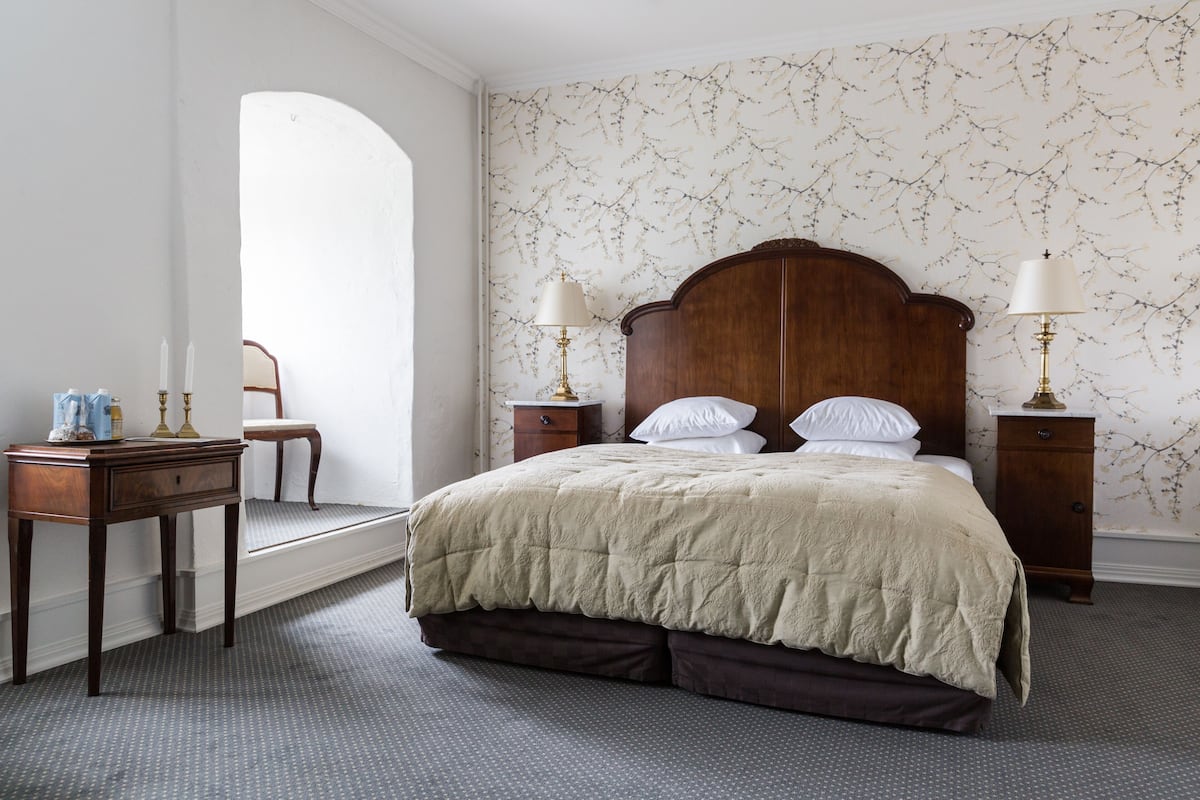 Une chambre à coucher avec un grand lit, deux tables de chevet avec des lampes, une petite table avec une lampe, une chaise et un miroir décoratif.