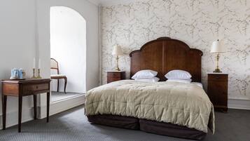A bedroom with a large bed, two bedside tables with lamps, a small table with a lamp, a chair, and a decorative mirror.
