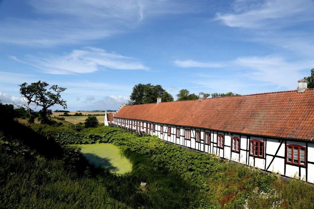 A traditional half-timbered building with a red-tiled roof, surrounded by lush greenery and a small pond.