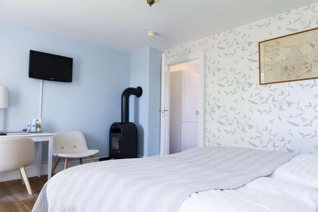 Een slaapkamer met een bed, een bureau met stoel, een zwarte heater en een televisie aan de muur.