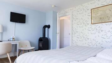 Een slaapkamer met een bed, een bureau met stoel, een zwarte heater en een televisie aan de muur.