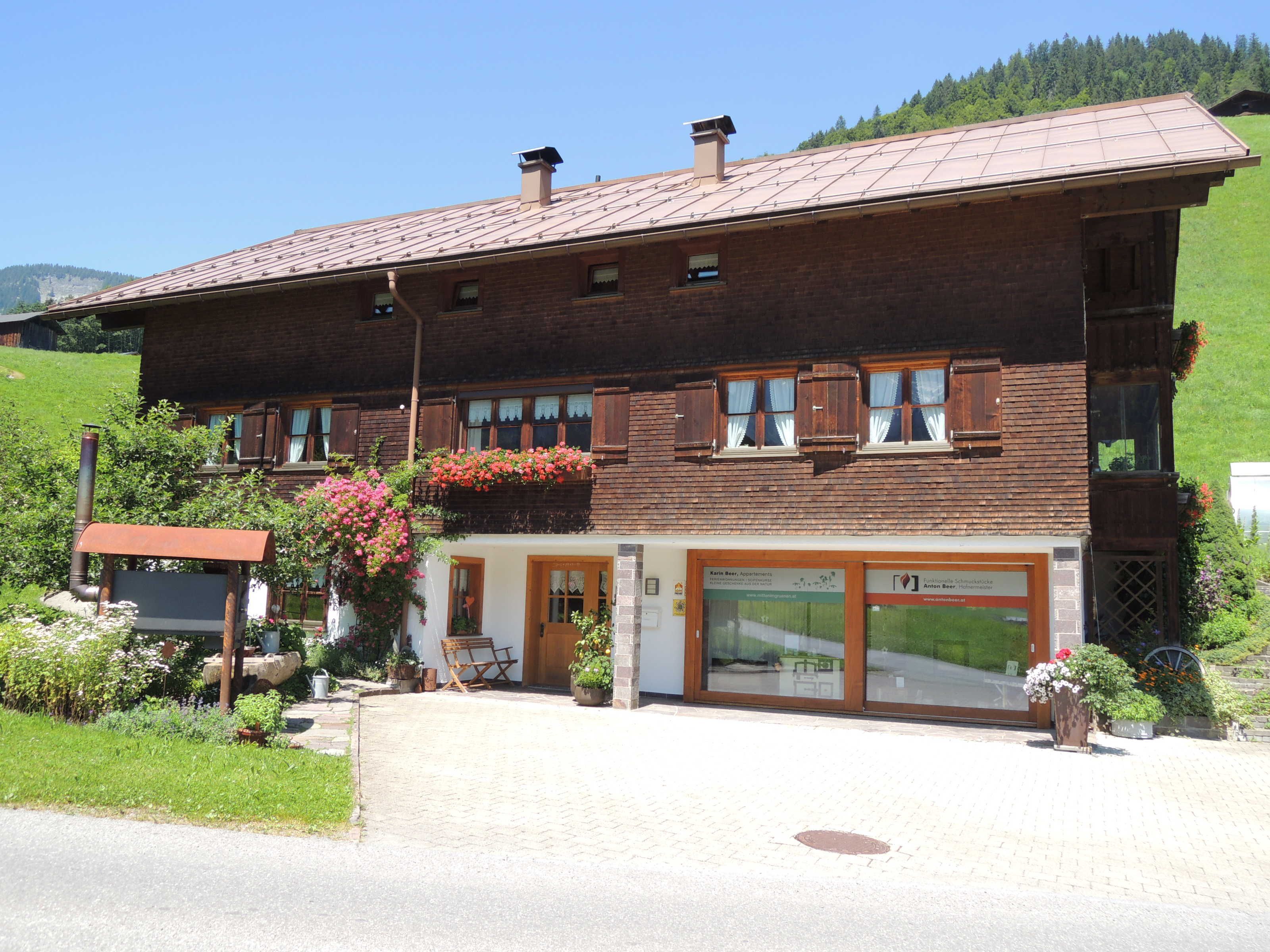 A two-story building with a brick facade, wooden shutters, and a balcony with flowers.
