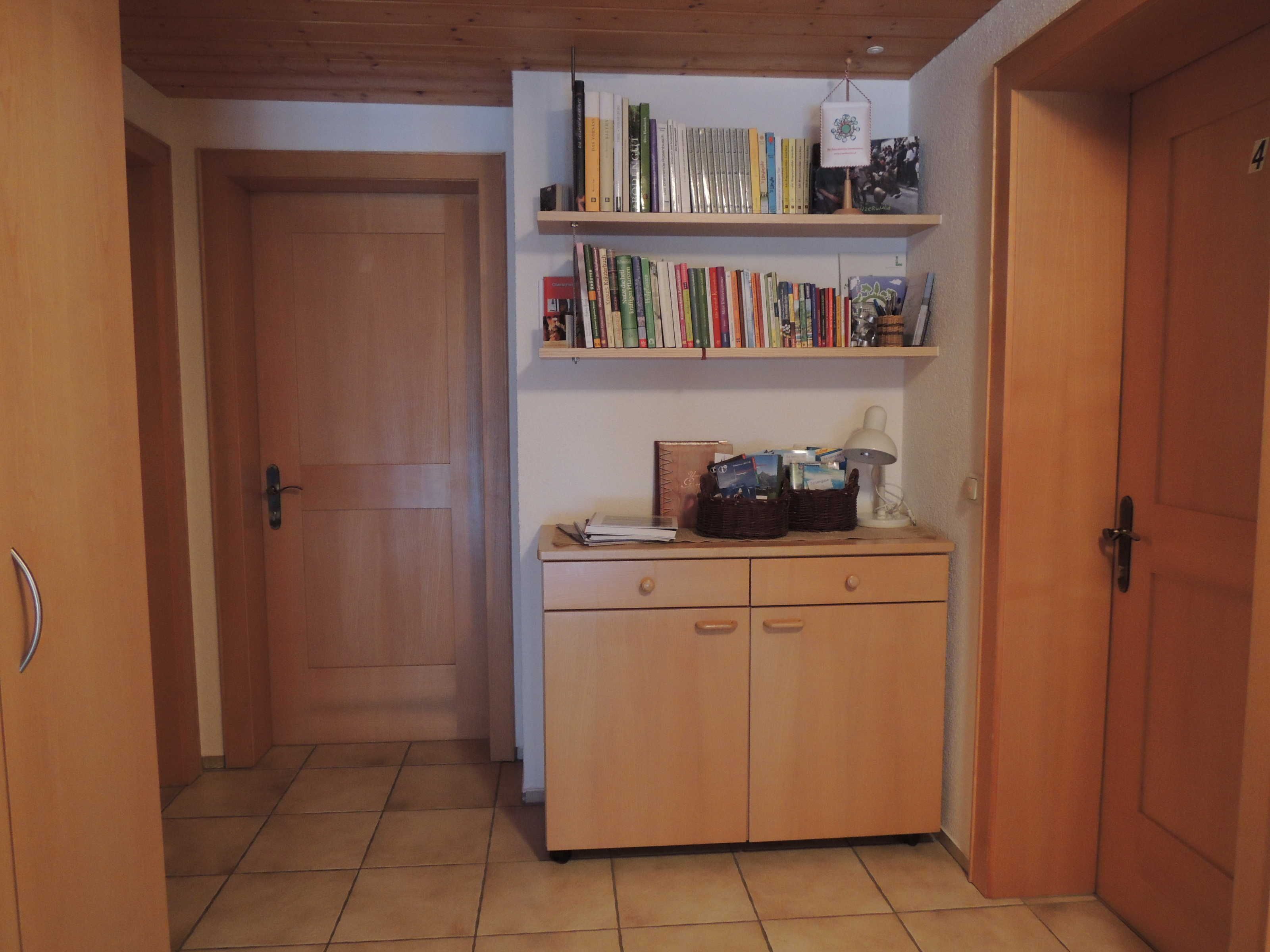 A hallway with wooden doors, a tiled floor, and a bookshelf with books and a lamp.