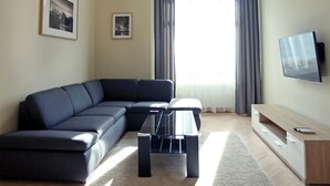 Ein modernes Wohnzimmer mit einem Ecksofa, einem Flachbildfernseher und einem großen Fenster mit Vorhängen.