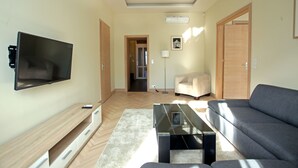 Ein modernes Wohnzimmer mit Flachbildfernseher, einer Couch, einem Couchtisch und einer Lampe.