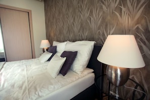 A neatly made bed with white and purple pillows, a bedside lamp, and a wall with a bamboo pattern. - Dfive Apartments - Splendor (Budapest)