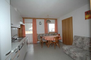 A compact kitchen with a dining table and chairs, a sofa, and a wooden door. - Studio apartment - House Luxer (Auffach)
