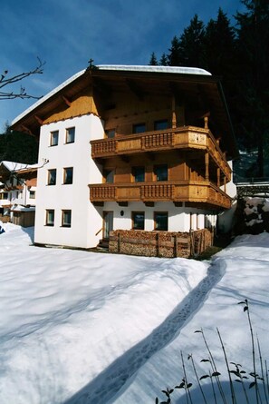 Un immeuble à plusieurs étages doté de balcons, un sol recouvert de neige et un paysage boisé en arrière-plan.