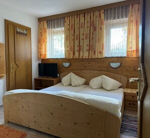 A wooden bed with a headboard, two bedside tables, a television on a stand, and a window with patterned curtains.