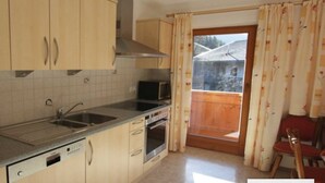 A kitchen with wooden cabinets, a microwave, a sink, and a view of a wooden deck through a door. - Studio apartment - House Luxer (Auffach)