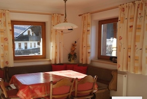 A dining area with a table, chairs, a bench, and a view of a building outside. - Studio apartment - House Luxer (Auffach)