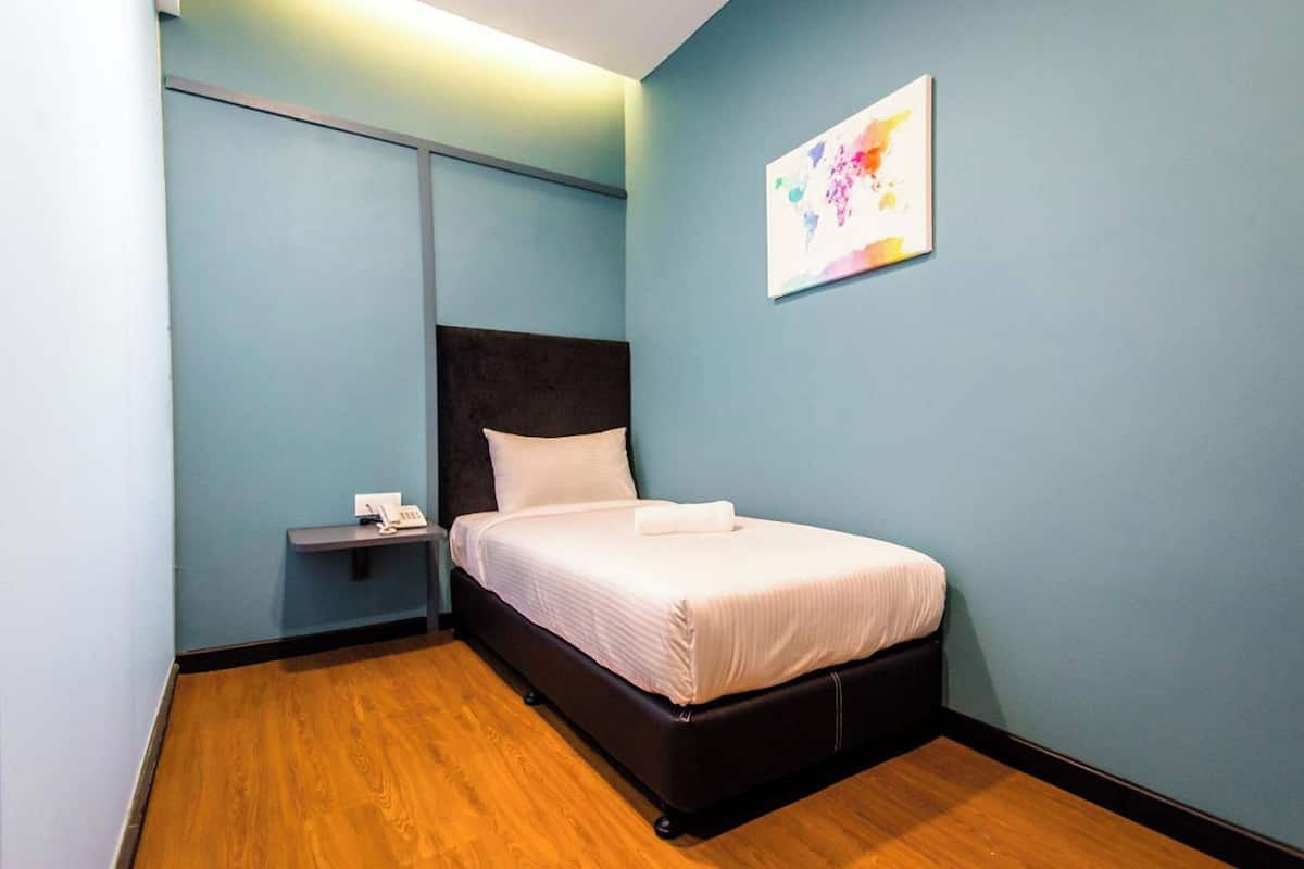 A single bed with a dark headboard in a room with light blue walls and wooden flooring.