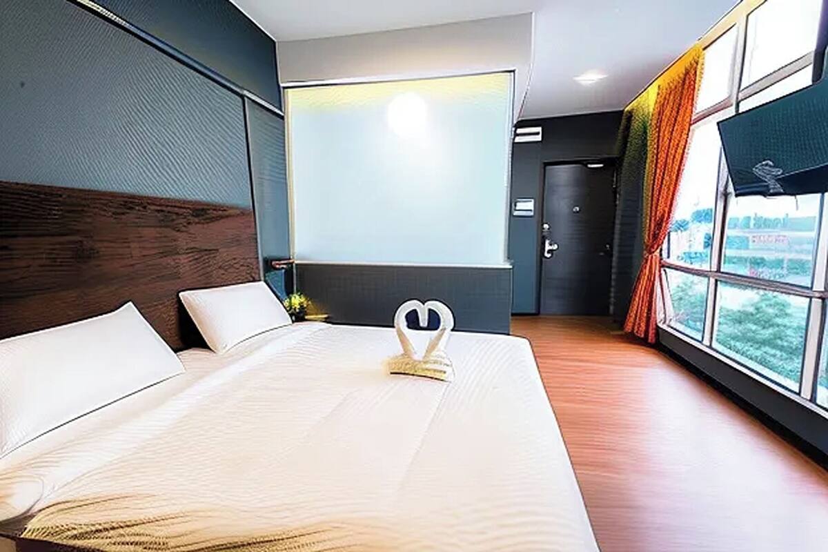 A hotel room with a large bed, a flat-screen TV, and a view of the outdoors through the windows.