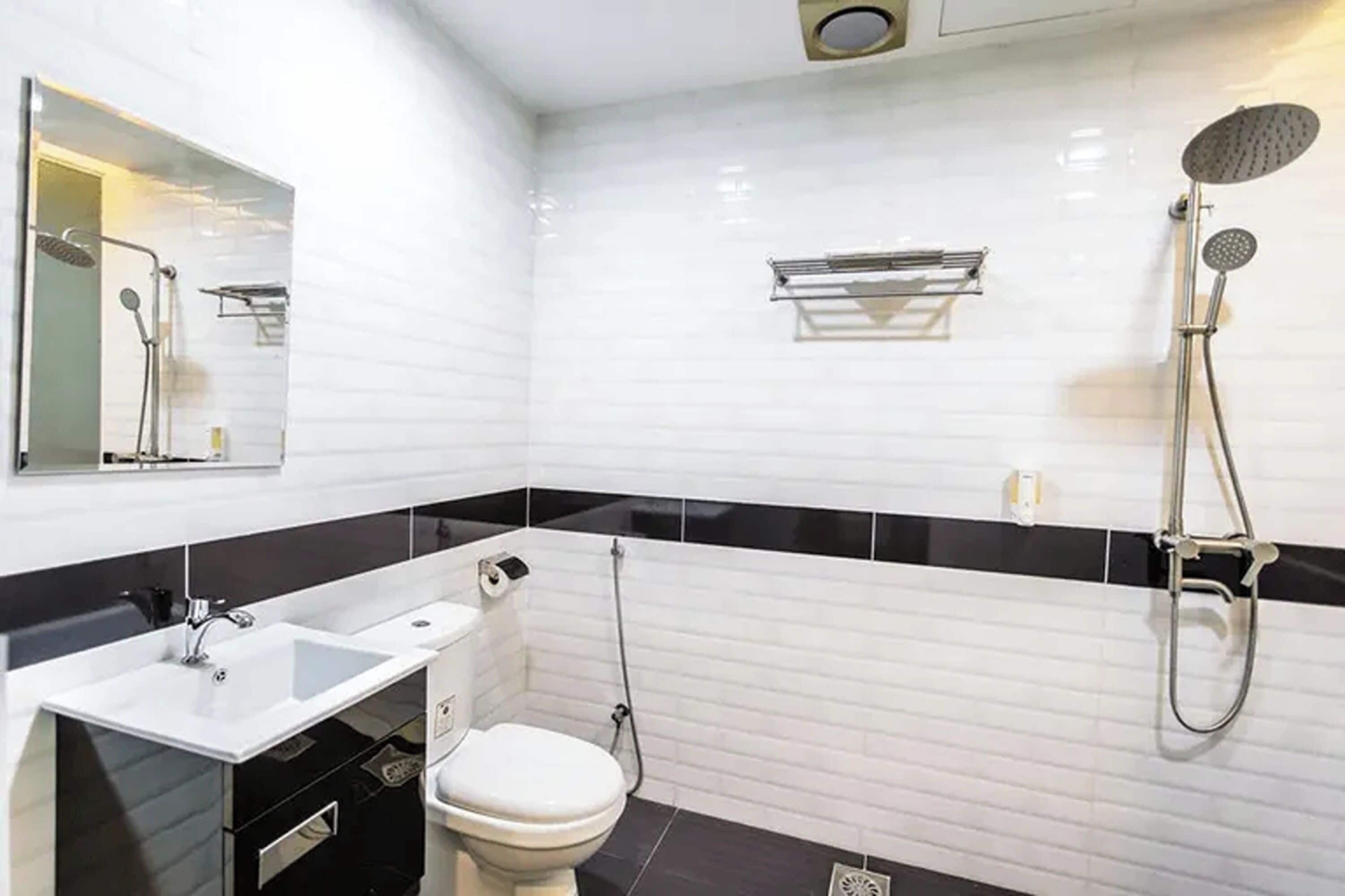 Un baño moderno con salpicadero de azulejos blancos y negros, un lavabo blanco, un inodoro y una ducha con cabezal de ducha de mano.