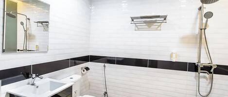 Un baño moderno con salpicadero de azulejos blancos y negros, un lavabo blanco, un inodoro y una ducha con cabezal de ducha de mano.