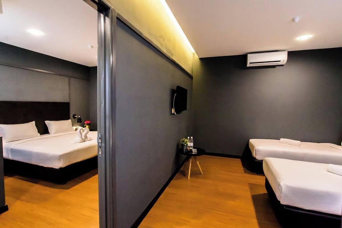 A hotel room with two beds, a small table with a vase, and an air conditioning unit on the wall.