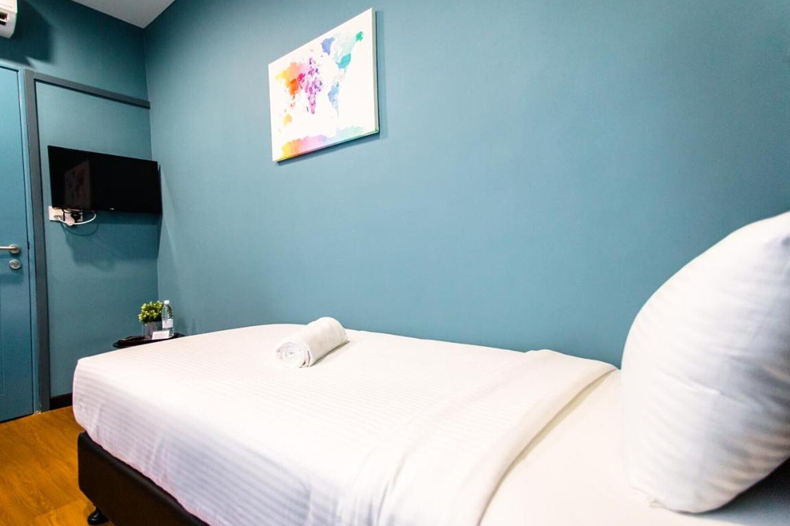 A hotel room with a bed, a flat-screen TV mounted on the wall, a small table with a plant, and a door.