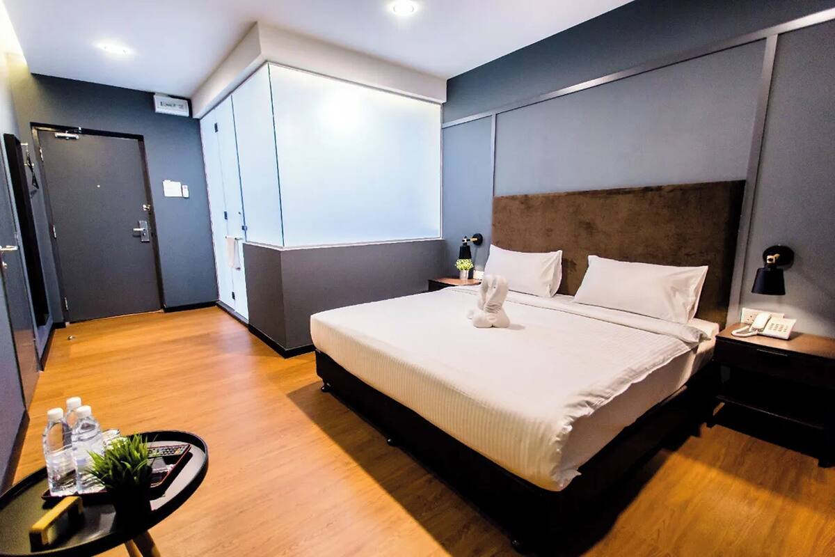 A hotel room with a large bed, a bedside table with a lamp, a small table with toiletries, and a wardrobe.