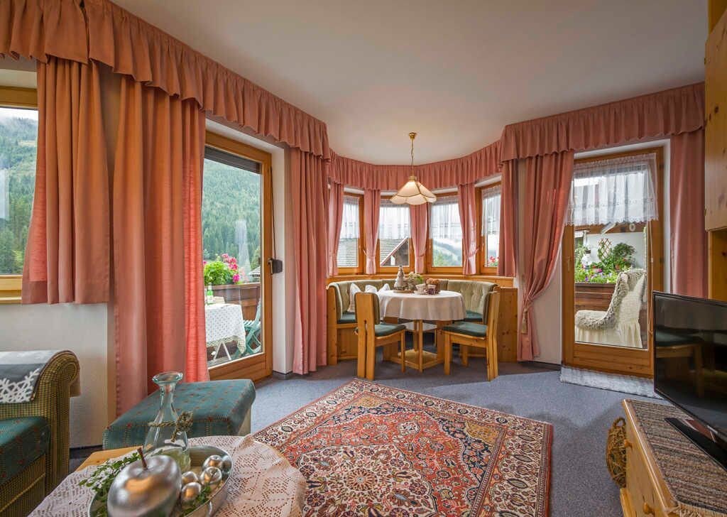 Een kamer met een eettafel, stoelen, een televisie en een groot raam met gordijnen.